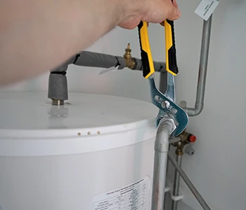 A person using pliers to fix a water heater.