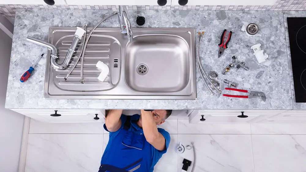 A plumber fixing a sink in a kitchen.