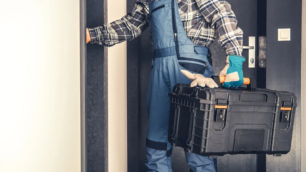 A plumber holding a tool case in front of a door.