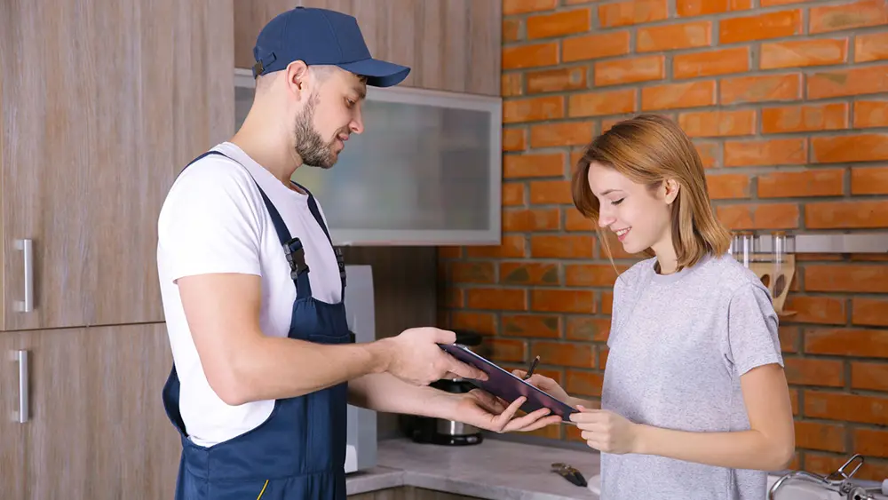 A man and a woman standing next to each other in a kitchen, discussing plumbing.