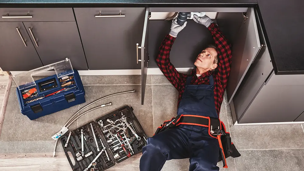 A plumber performing plumbing work under a kitchen sink.